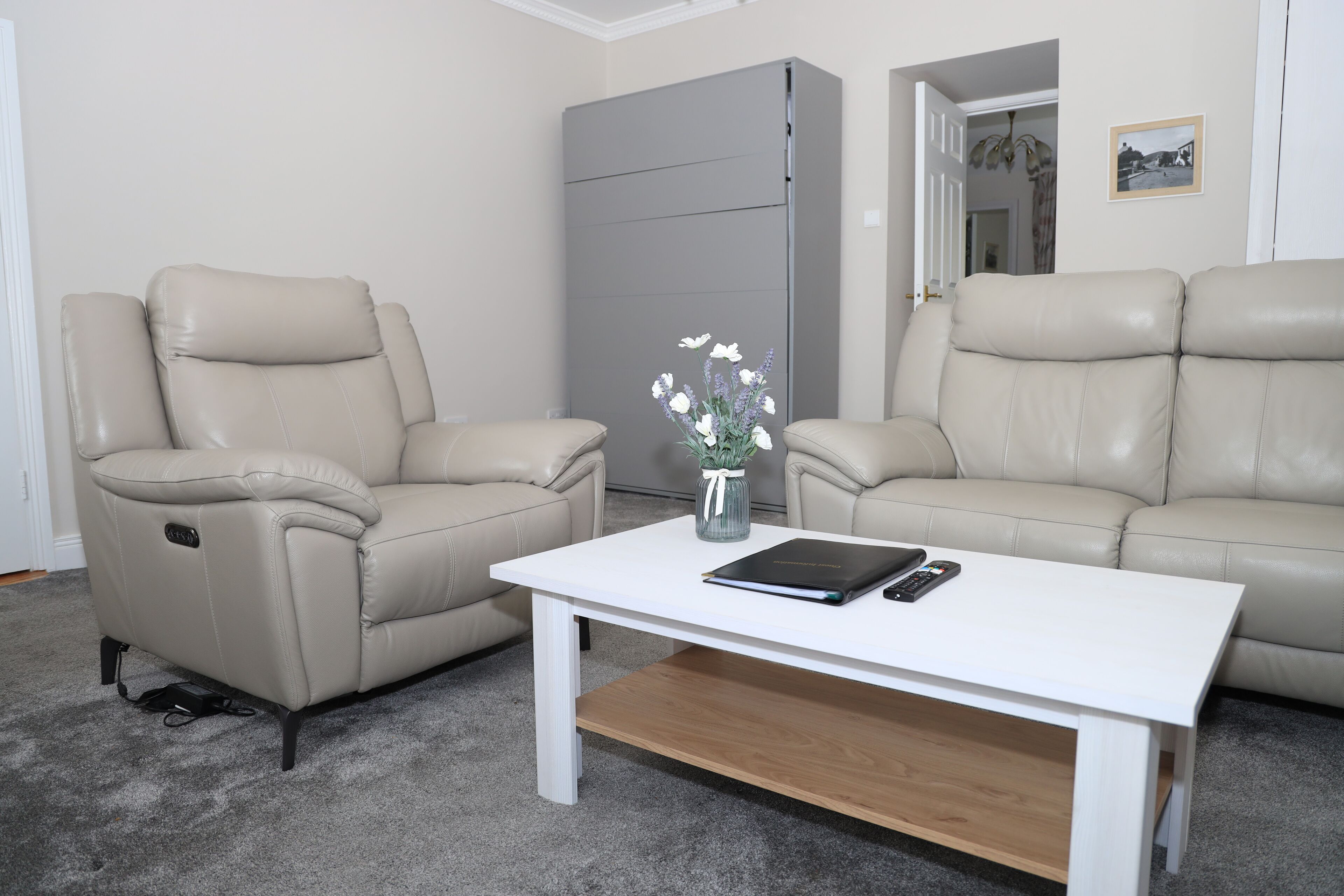 A living room with two beige leather recliners, a white coffee table with a book and remote, and a gray cabinet.