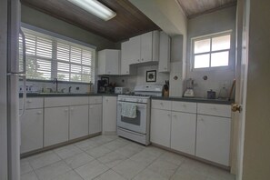 A kitchen with white cabinets, a stove, and a window with blinds.