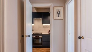 A hallway leading to a kitchen with dark cabinets, a stove, and an oven. - 2-bed Flat Near Marylebone High Street · Sleeps 4 (London)