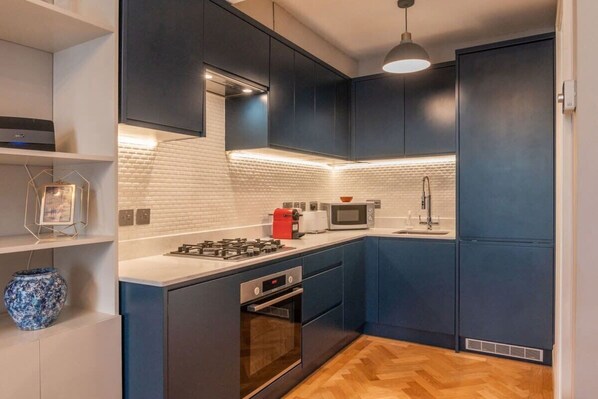 Una cocina moderna con armarios oscuros, una encimera blanca, una estufa a gas, un microondas y un tostador rojo.