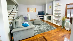 A living room with a grey sofa, a TV, a fireplace, and a staircase. - Casa com espaço gourmet, home office e 3 suítes \- Granja Viana (Carapicuiba)
