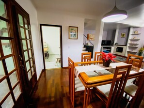 A dining area with wooden chairs and a table, a kitchen in the background, and a staircase leading to another room. - Casa com espaço gourmet, home office e 3 suítes \- Granja Viana (Carapicuiba)