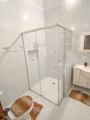 A modern bathroom with a glass shower enclosure, a toilet with a leopard print seat cover, and a vanity with a mirror. - Casa com espaço gourmet, home office e 3 suítes \- Granja Viana (Carapicuiba)
