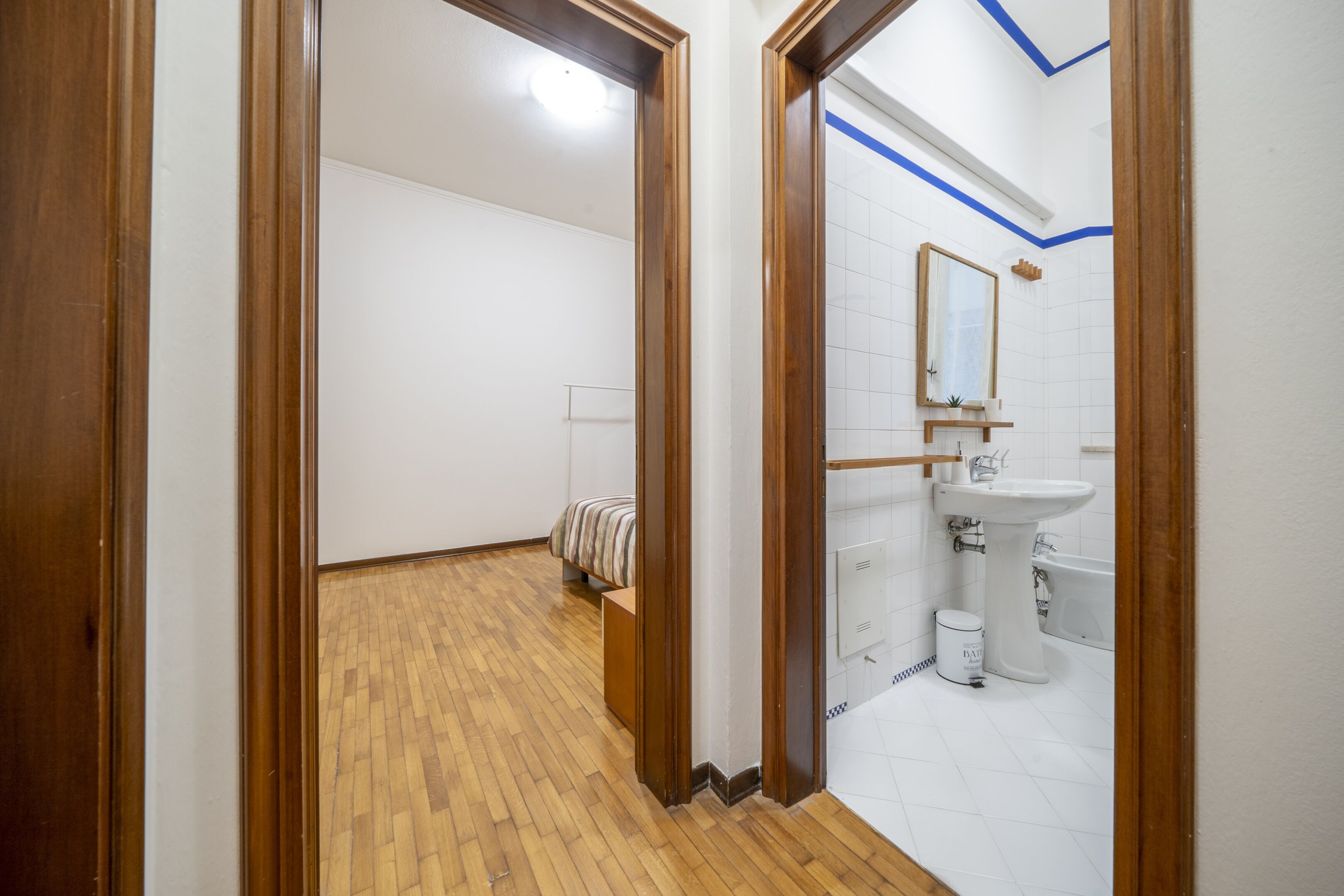 Un couloir doté d’un plancher en bois qui mène à une salle de bain avec un lavabo et un miroir.