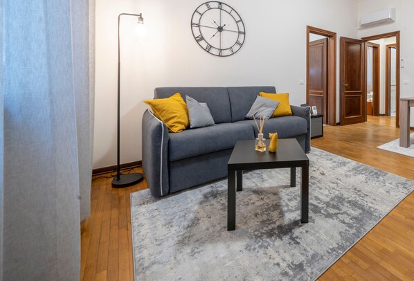 A modern living room with a grey sofa, yellow cushions, a black coffee table, and a large wall clock. - [Ghirlandina]Fabulous apartment in the city center (Modena)