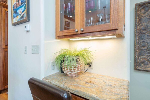 Una cocina con armarios de madera, encimera de granito, una planta en maceta y una lámpara fijada a la pared.
