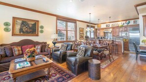 Un vaste salon comprenant un canapé, des fauteuils et une table basse, qui donne sur une cuisine avec des meubles en bois et un coin repas.