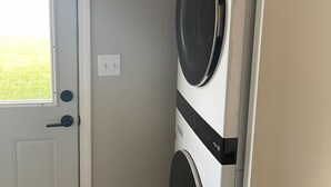 Une buanderie équipée d’un lave-linge et d’un sèche-linge à chargement frontal, d’une porte avec une fenêtre et d’un interrupteur sur le mur.
