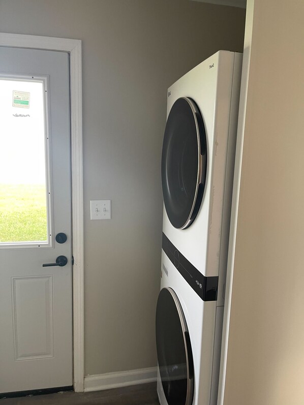 A laundry room with a front-loading washer and dryer, a door with a window, and a light switch on the wall.