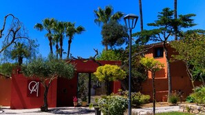 A red building with a white logo, surrounded by palm trees and greenery. - Quinta dos Amigos (Loulé)