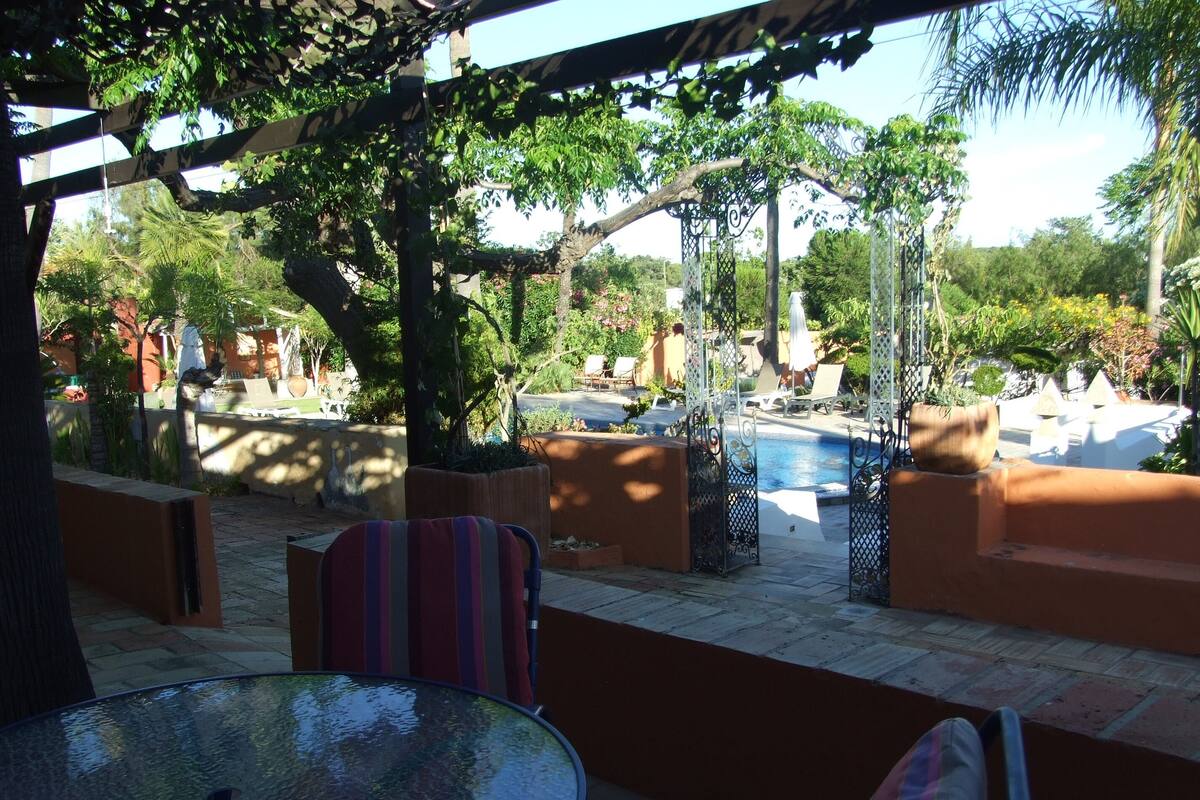 Un espacio al aire libre techado con piscina, sillas de descanso y una mesa de vidrio.