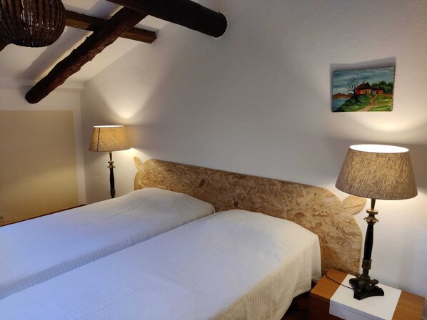 A bedroom with two beds, wooden headboard, two wall-mounted lamps, and a painting on the wall. - Quinta dos Amigos (Loulé)