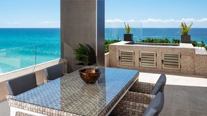 Ein Balkon mit Glasgeländer und Meerblick, ausgestattet mit Tisch, Stühlen und Blumentöpfen.