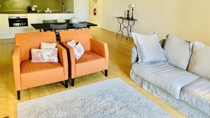 Una sala de estar moderna con un sofá, dos sillones, una mesa de comedor y una cocina al fondo.