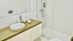 Un baño moderno con un lavamanos blanco, cabina de ducha con mampara de vidrio y un inodoro.