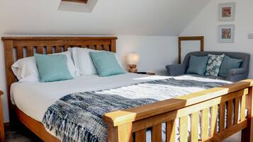 A bedroom with a wooden bed, a grey sofa, a small table with a lamp, and a skylight above the bed.