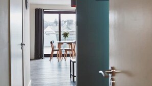 Une chambre d’hôtel offrant une vue sur le paysage urbain grâce à de grandes fenêtres, un coin repas avec une table et des chaises, et un design moderne agrémenté d’un mur d’accent de couleur turquoise.