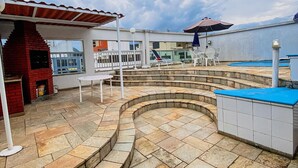A rooftop pool area with a curved stone design, a barbecue, and outdoor seating.