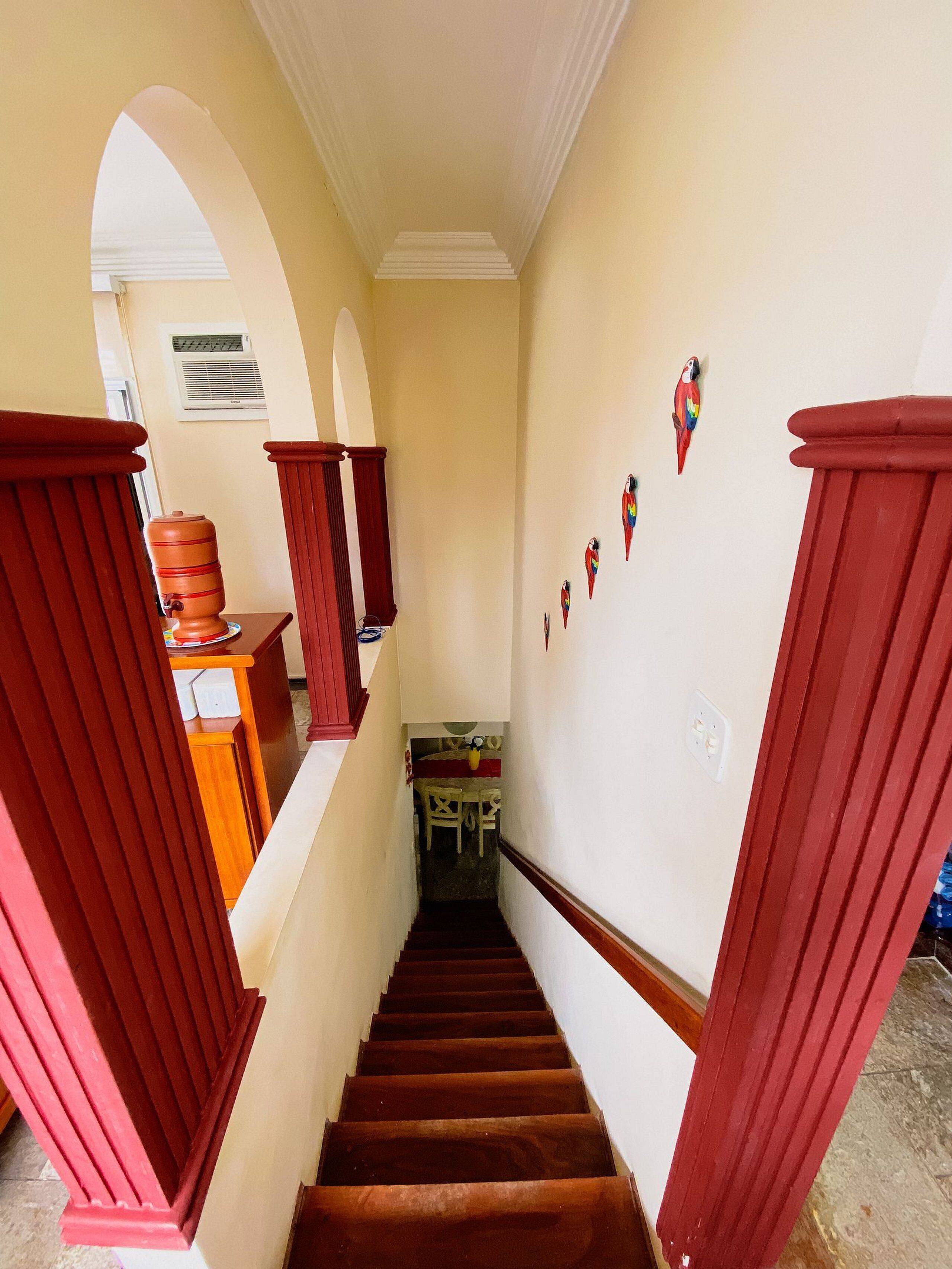 Un escalier étroit avec des rampes rouges et un mur blanc orné d’éléments décoratifs.