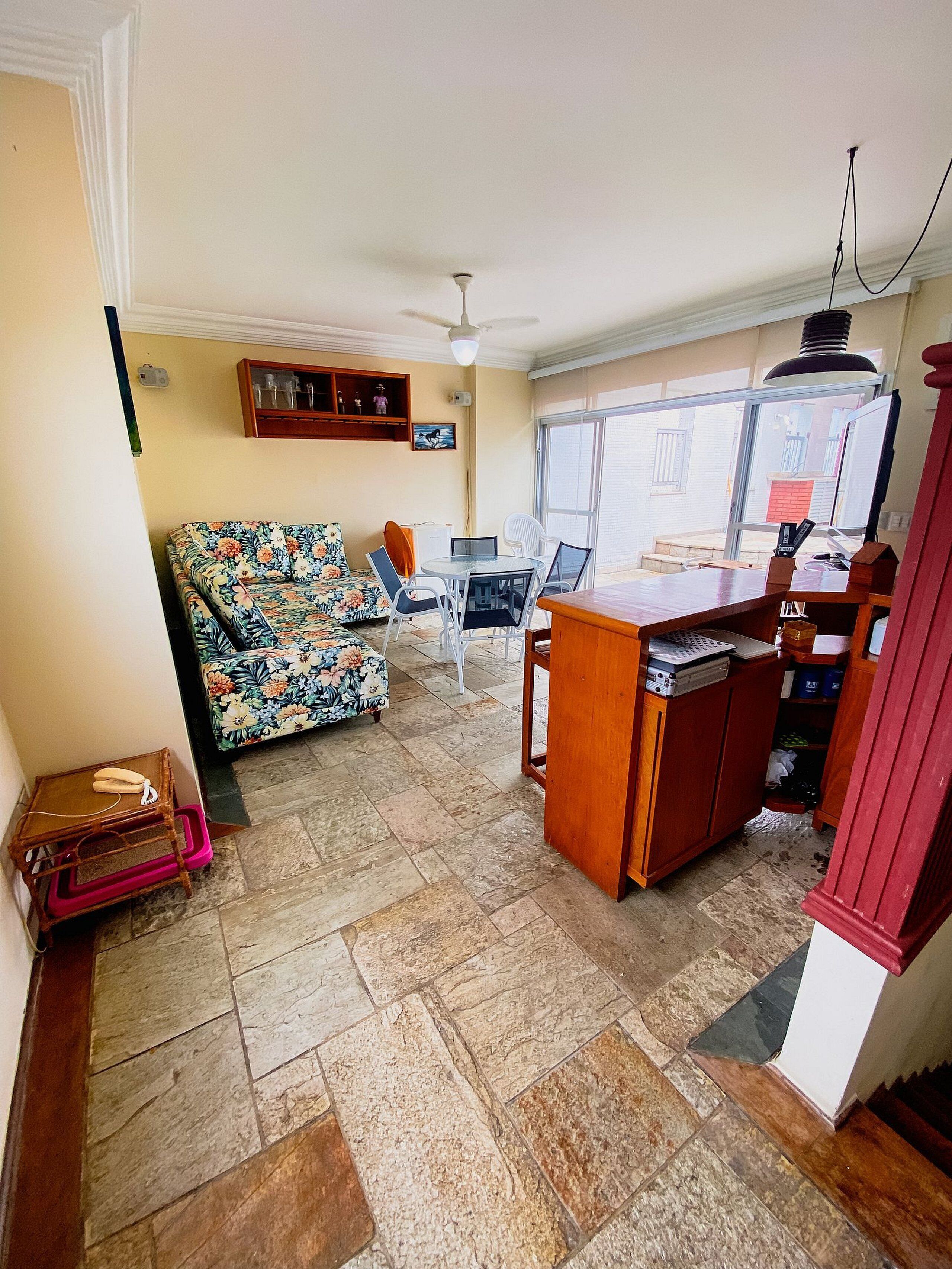 Uma sala de estar com sofá estampado, mesa de jantar com cadeiras, armário de madeira e ventilador de teto.