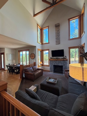 A spacious living room with a fireplace, a television, and multiple windows offering views of the outdoors.