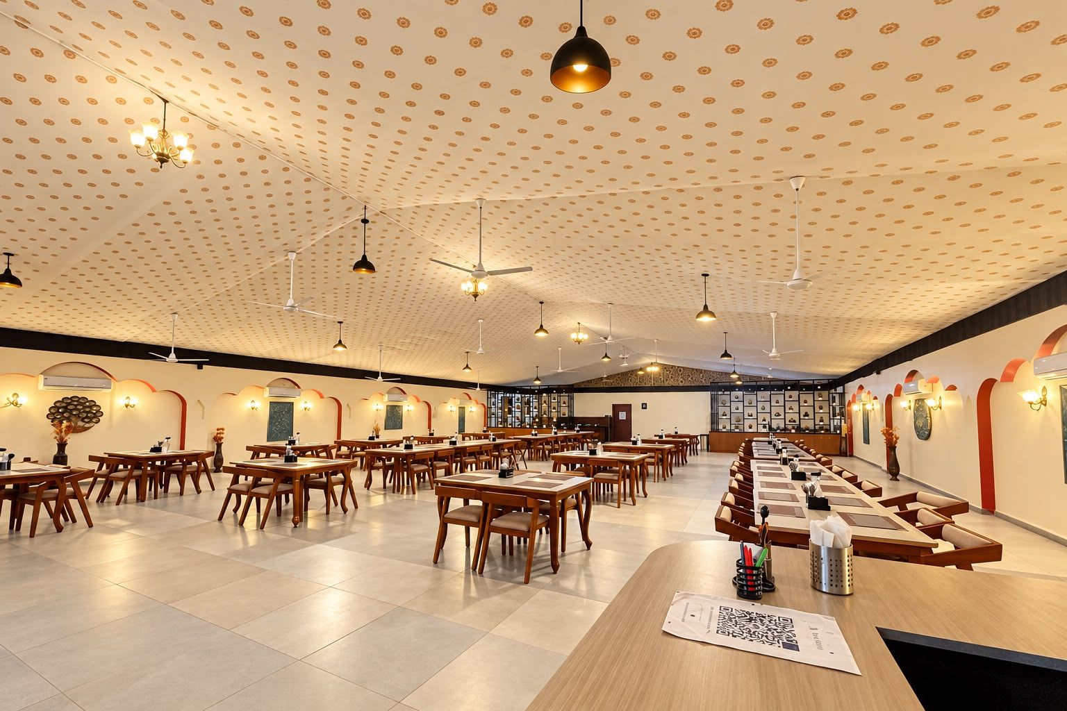 Un comedor amplio con varias mesas y sillas, ventiladores de techo e iluminación colgante.