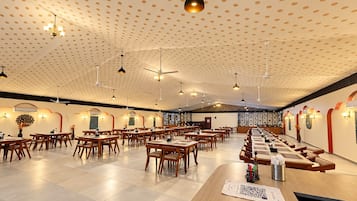 Un comedor amplio con varias mesas y sillas, ventiladores de techo e iluminación colgante.