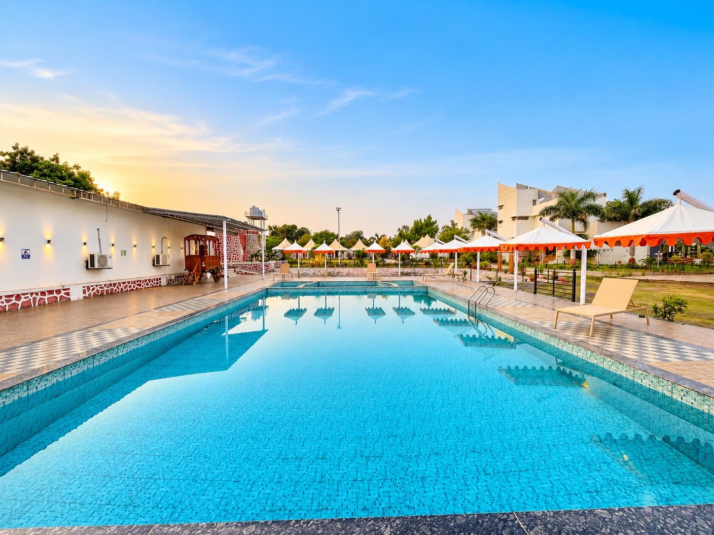 A swimming pool with lounge chairs and umbrellas, surrounded by buildings and greenery.