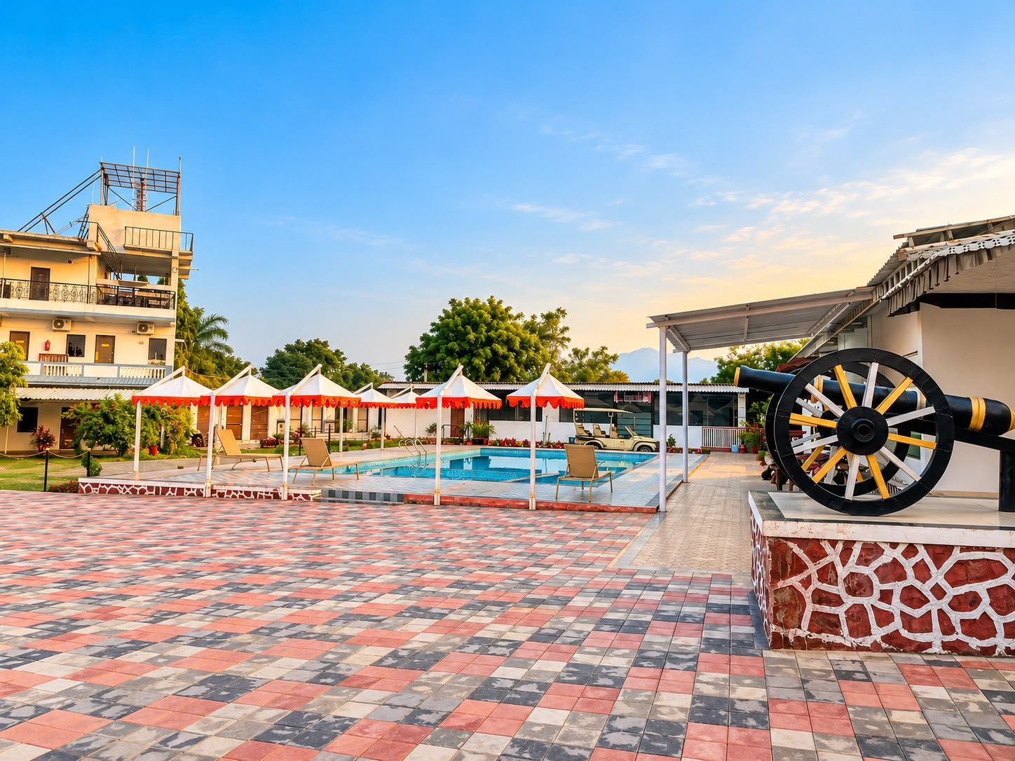 Zona de piscina con suelo de baldosas, sombrillas y una fuente.