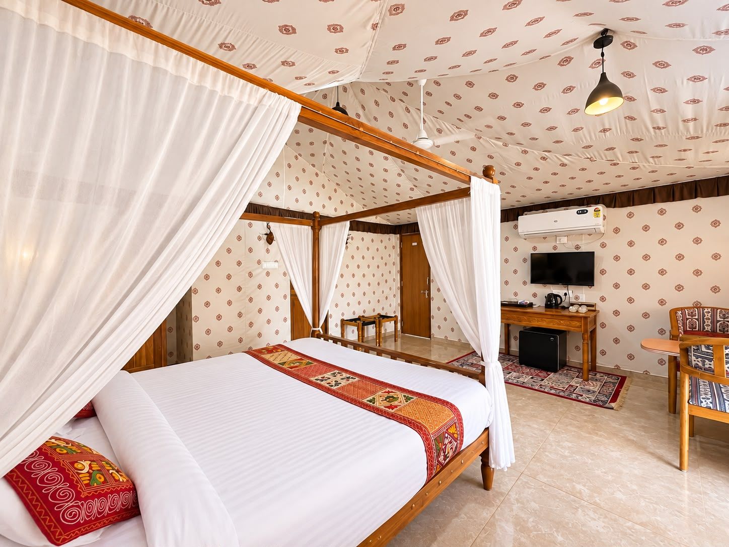 A four-poster bed with a canopy, a television, a desk, and a chair in a room with patterned wallpaper.