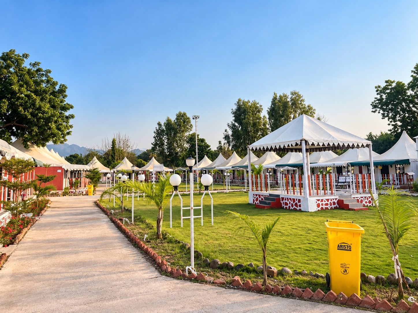 A pathway leading to a series of white tents with red accents, surrounded by greenery and a clear sky.