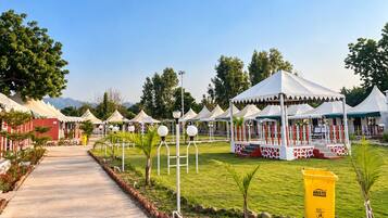 A pathway leading to a series of white tents with red accents, surrounded by greenery and a clear sky.