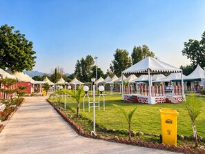 A pathway leading to a series of white tents with red accents, surrounded by greenery and a clear sky. - Vasant Vihar Resort (Garudeshwar)