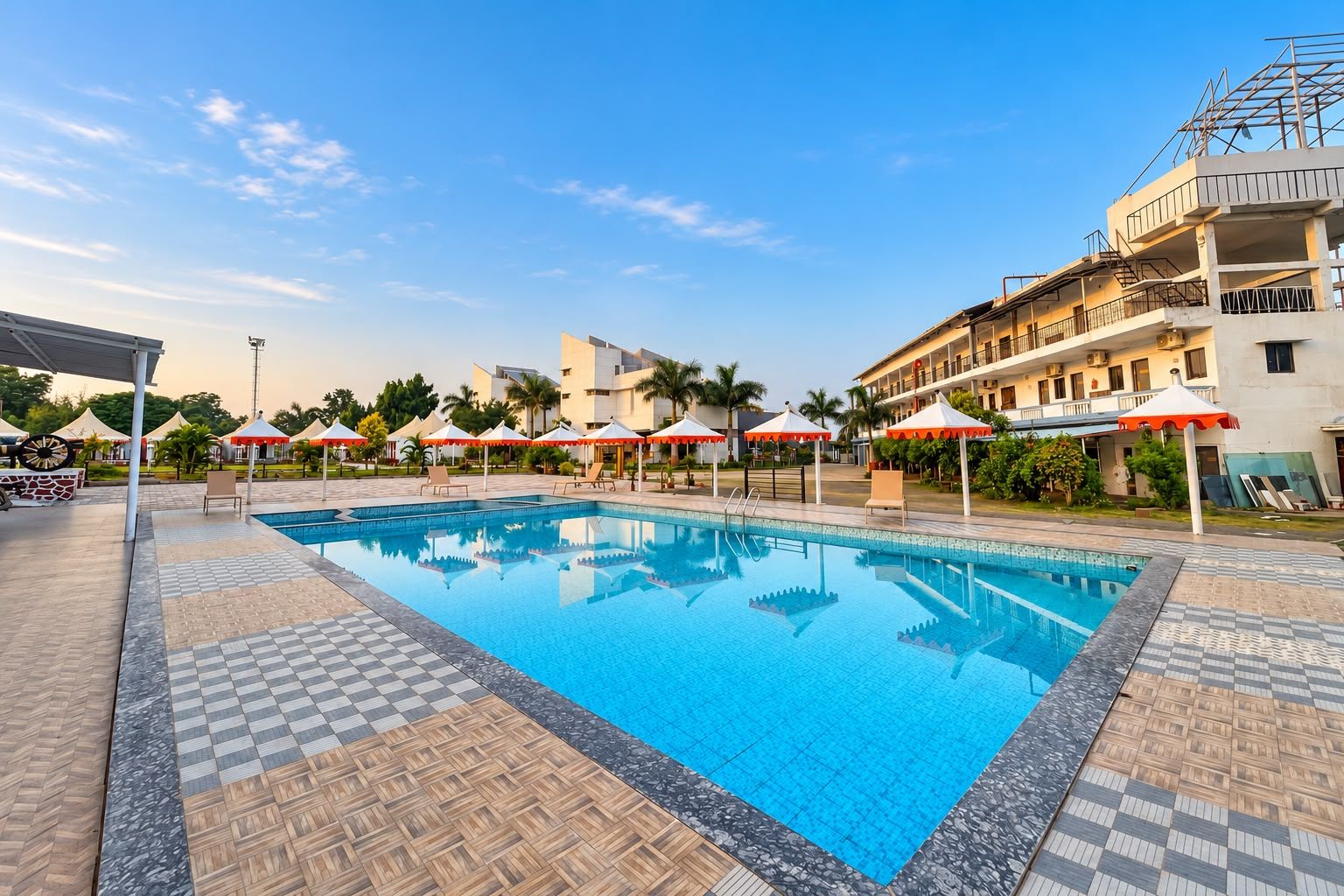 A swimming pool with lounge chairs and umbrellas, surrounded by a building with multiple floors and balconies.