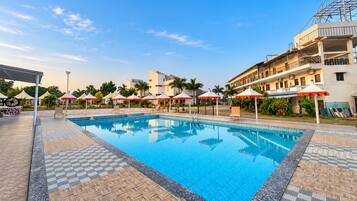 A swimming pool with lounge chairs and umbrellas, surrounded by a building with multiple floors and balconies.
