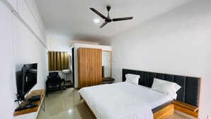 Una habitación de hotel moderna con una cama grande, un escritorio con computadora, un televisor y un ventilador de techo.