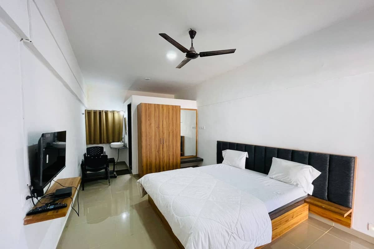 Una habitación de hotel moderna con una cama grande, un escritorio con computadora, un televisor y un ventilador de techo.