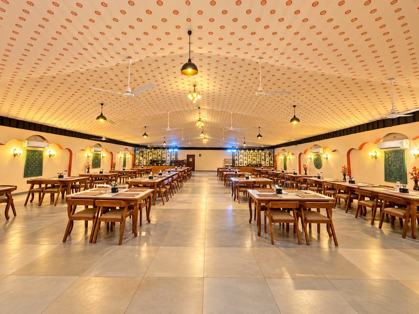 Une salle à manger spacieuse, dotée de nombreuses tables et chaises, de ventilateurs de plafond et de luminaires suspendus.