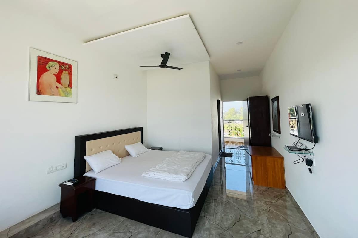 Un dormitorio con cama, ventilador de techo, televisor y puerta que da a un balcón.