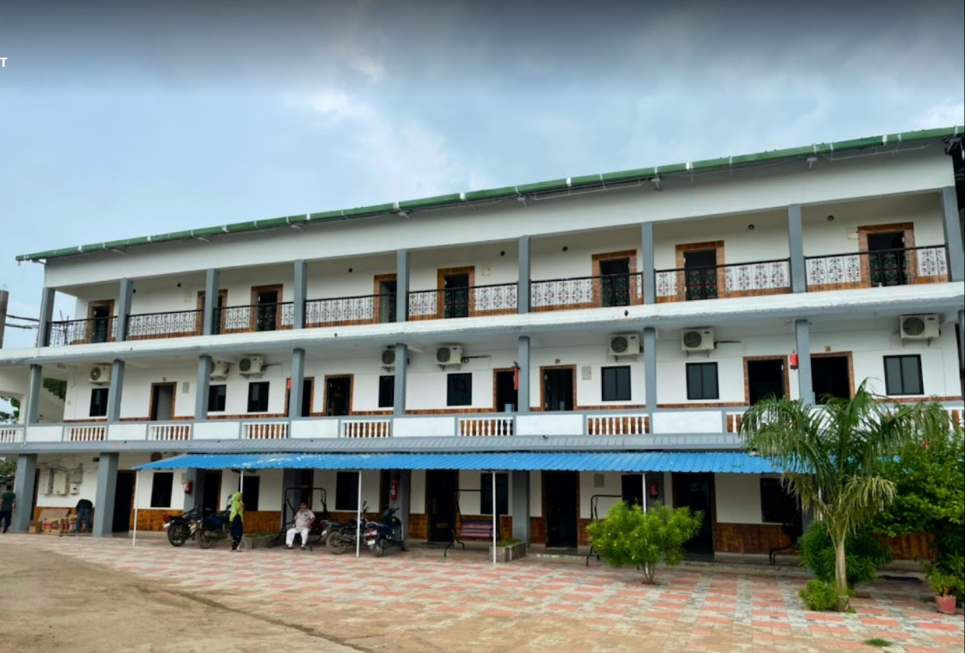 A multi-story hotel with a flat roof, balconies, and a covered outdoor area with a blue awning.
