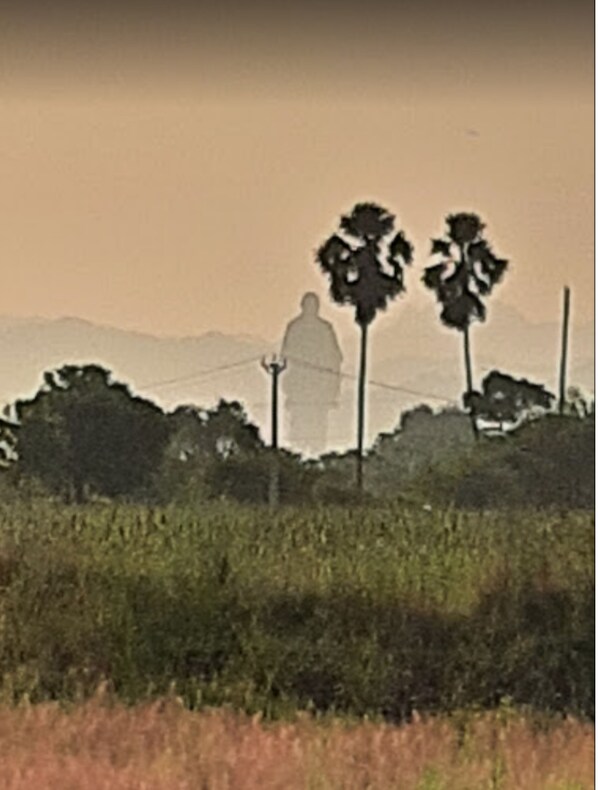 Uma paisagem com um edifício grande, possivelmente um monumento ou torre, rodeado de árvores e vegetação.