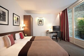 Une chambre d’hôtel avec deux lits, un bureau, une télévision et une grande fenêtre avec des rideaux.