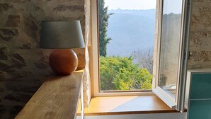 A rustic wooden table with a towel and a black object, a stone wall, and a window with a view of greenery and hills. - The Dovecote (REILHAGUET)