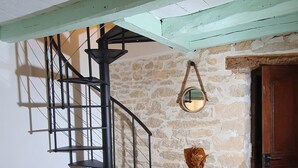A spiral staircase with a black metal railing, a stone wall, and a wooden counter with a green vase and a white cloth. - The Dovecote (REILHAGUET)