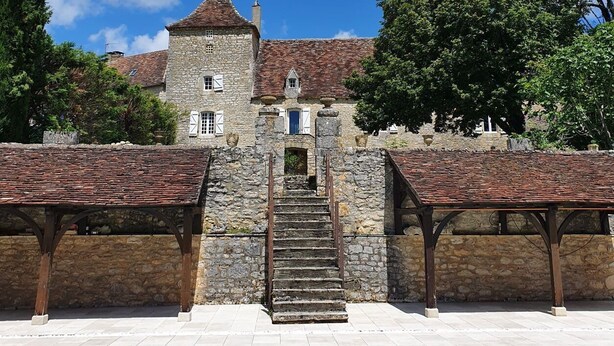 A stone building with a staircase leading to a door, surrounded by trees and a clear blue sky. - The Dovecote (REILHAGUET)