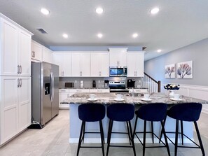 A modern kitchen with white cabinets, stainless steel appliances, and a marble island with bar stools.