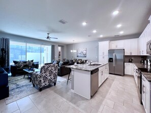 A modern kitchen with white cabinetry, a central island, and a dining area with a sofa and chairs.