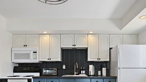 A modern kitchen with white cabinets, a black herringbone backsplash, a blue countertop, and a white refrigerator.