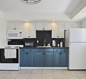 Cocina moderna con armarios blancos, un salpicadero de color negro tipo espiga, encimera azul y refrigerador blanco.