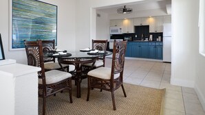 A dining area with a round table and six chairs, a kitchen with blue cabinets and white appliances, and a large abstract painting on the wall.